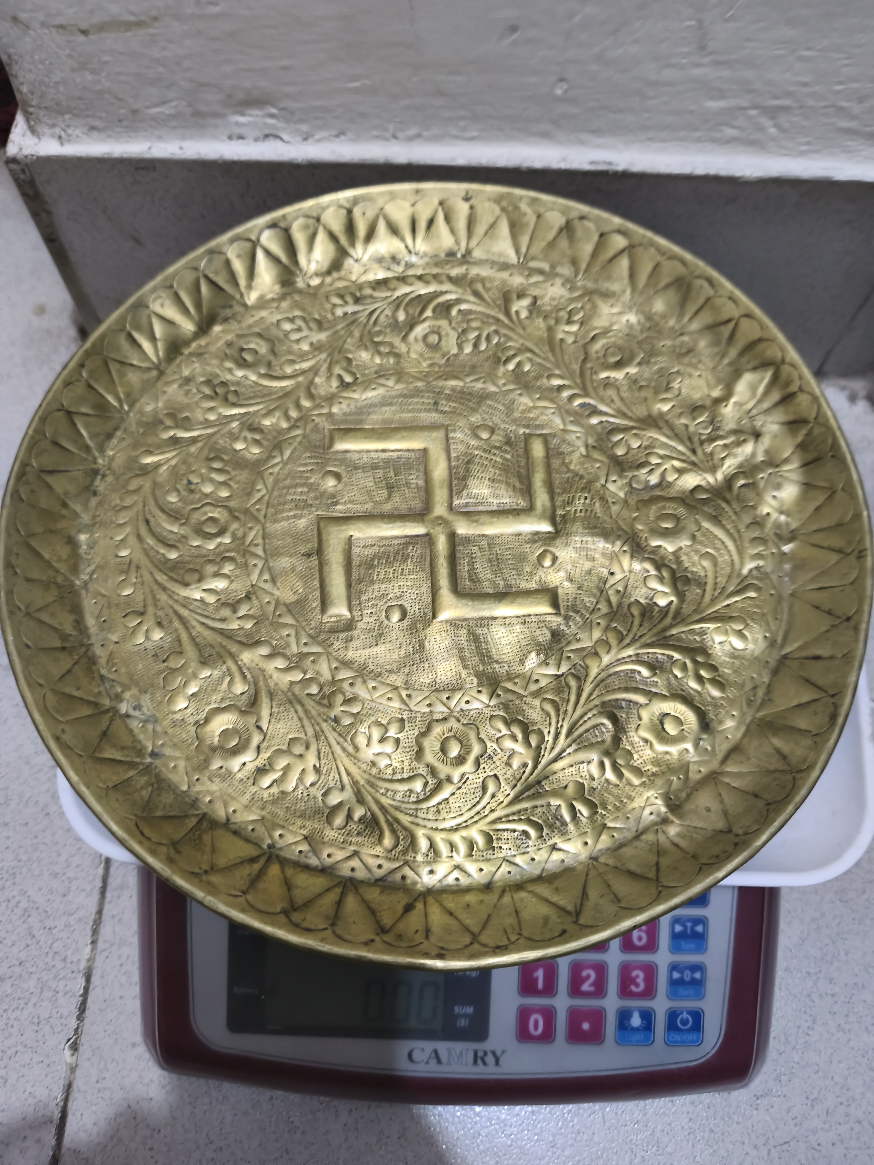 একটি আলংকারিক পিতলের পূজার থালি যাতে ফুলের নকশা দ্বারা বেষ্টিত একটি খোদাই করা স্বস্তিক প্রতীক